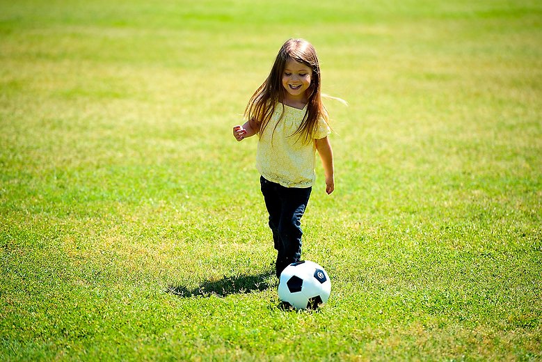 Flicka som spelar fotboll på grönt gräs